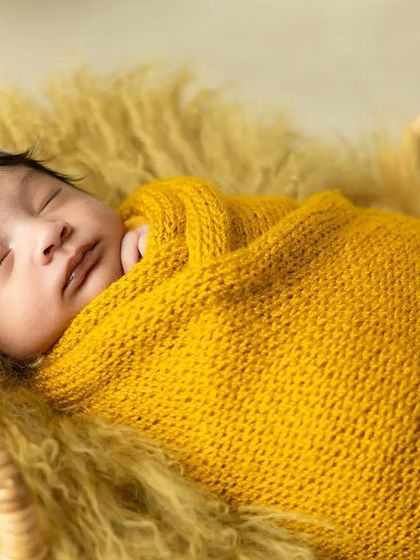A peaceful newborn wrapped snugly in a yellow knit blanket, dreaming sweetly. I use soft textures and warm colors to create cozy and artistic newborn portraits.