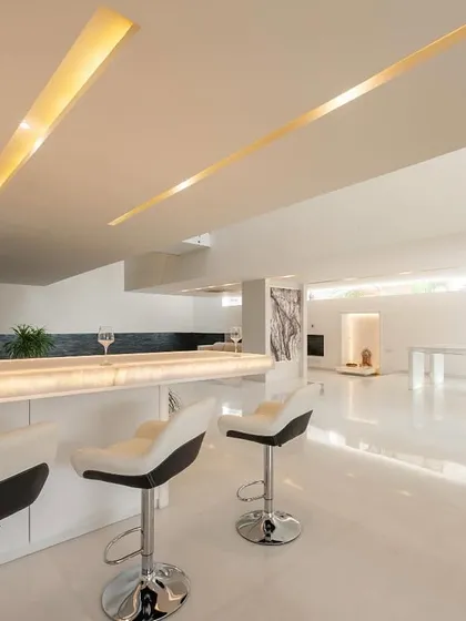 a custom-designed bar counter made of backlit white onyx, serving as a luminous focal point in an open-plan living area… the handle-less cabinetry maintains a clean, monolithic look.