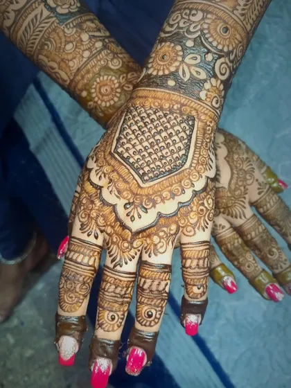 This design highlights a prominent geometric pattern on the back of the hand, framed by delicate scalloped edges. It's a modern take on traditional bridal henna.