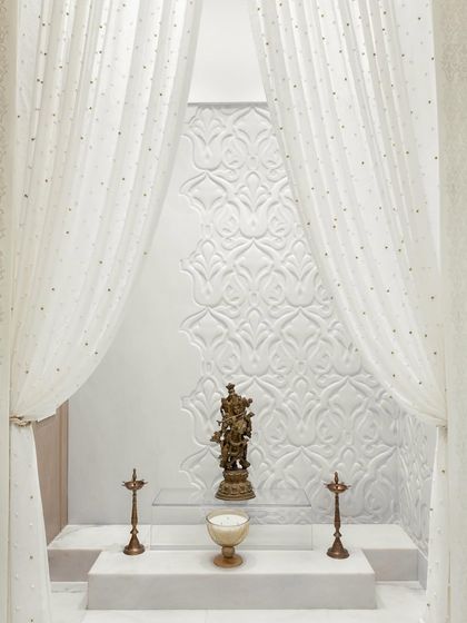 A full view of the all-white marble pooja room. The tiered platform, brass idols, and intricately carved backdrop come together to form a truly heavenly retreat for prayer and meditation.