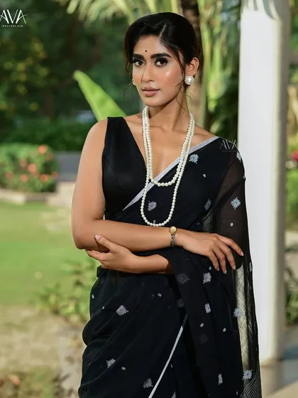 A close-up portrait of the model in the black saree, without sunglasses. Her direct gaze and the simple pearl necklace create a look of timeless sophistication and grace.