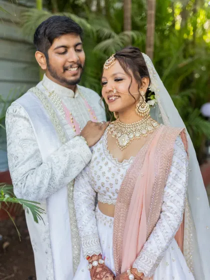 A romantic moment between the bride and groom. Her elegant white lehenga is paired with a delicate polki necklace, showcasing a soft and sophisticated bridal style.