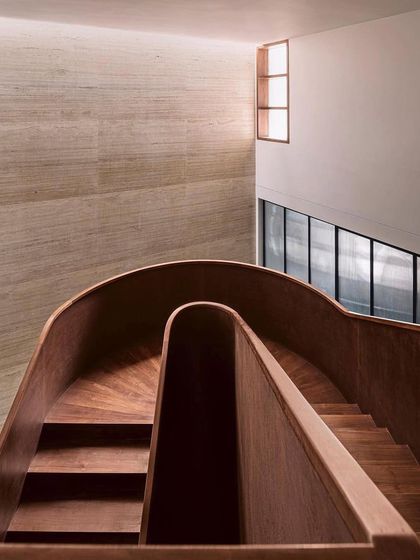 A detail of the internal wooden staircase, where the fluid curves of the handrail and the warm texture of the wood create a sculptural and inviting path between floors.