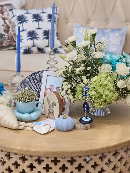 The central coffee table, featuring a lush floral arrangement, blue taper candles, and personalized items like a fan and a framed photo.