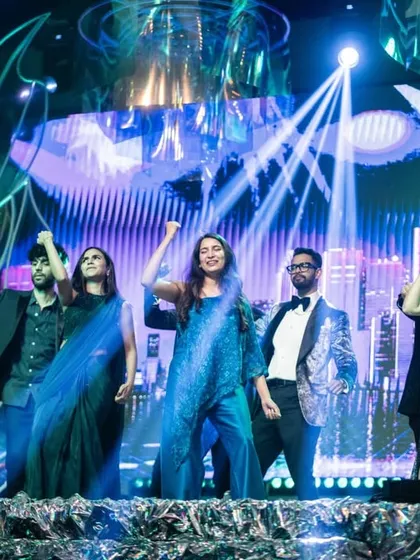 A group dance performance on the Sangeet stage, with a dynamic city skyline graphic on the LED screen behind them. The lighting is synchronized to the music to create an energetic and immersive experience.