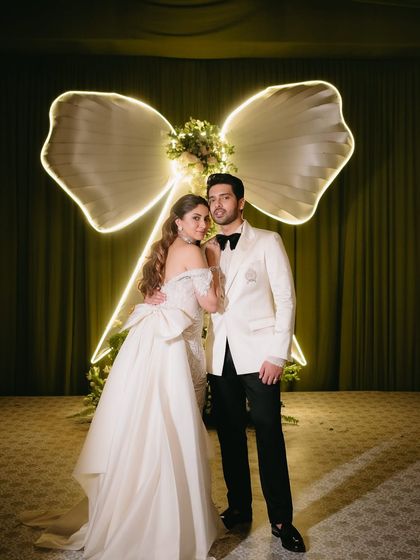 A classic portrait of the couple in front of the illuminated bow backdrop, a perfect memento from their "Big Bow Affair."