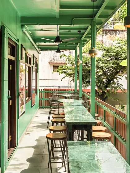 The open-air veranda of this cafe features long, green marble-topped counters for patrons to enjoy the view. The design extends the interior's color palette outwards, connecting the built space with the surrounding trees and creating a perfect spot for community gathering.