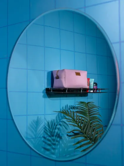 A creative shot of a pink pouch seen through the reflection of a round mirror against a blue tiled wall. This artistic composition is unique and memorable, perfect for a social media campaign.