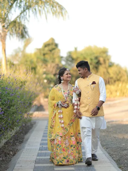 A beautiful shot of the couple walking together. The bride's floral jewellery adds a touch of elegance to her festive Haldi attire.