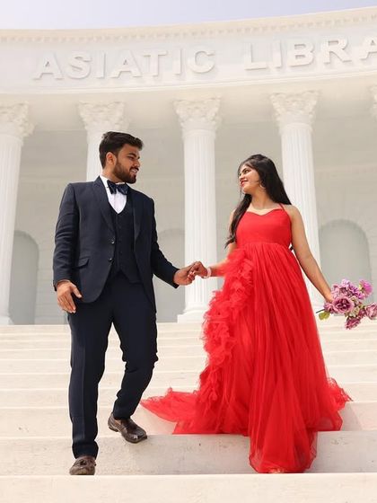 A grand pre-wedding shot on the steps of a beautiful white building. The red ruffled gown is a classic and elegant choice for such a location.