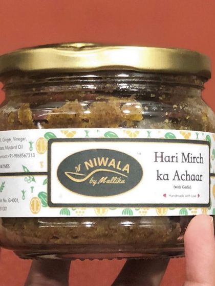 A hand holding a jar of my Hari Mirch ka Achaar with garlic. This version has an extra kick from the garlic, making it even more flavourful.