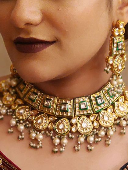 A close-up of a beautiful Kundan choker with green enamel and pearl drops. The craftsmanship is perfect for a bride who appreciates detail.