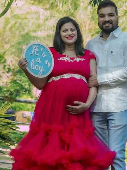 A classic gender reveal photo in a park setting. The couple proudly holds an "It's a boy" sign, sharing their happy news with friends and family.