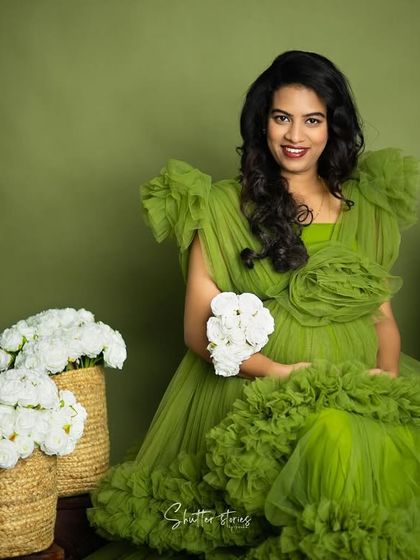 A joyful and direct portrait, with the mom-to-be smiling at the camera, holding a small bouquet of white flowers.