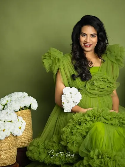 A joyful and direct portrait, with the mom-to-be smiling at the camera, holding a small bouquet of white flowers.