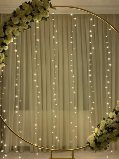 A simple and elegant golden hoop with a fairy light curtain. The arch is adorned with two beautiful bouquets of artificial white roses, perfect for an engagement or anniversary.