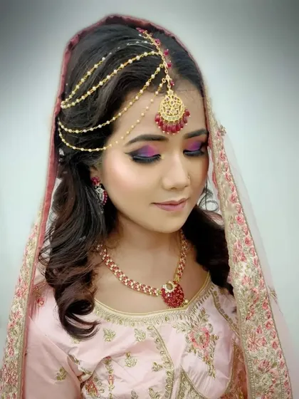 The soft pink and purple eyeshadow tones are blended perfectly to complement the bride's pastel pink lehenga.