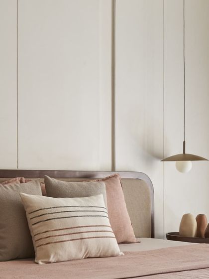 The pendant light and striped cushion add subtle details to this minimalist bedroom. The focus is on soft textures and a muted color palette to create a restful environment.