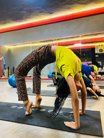 A student in Chakrasana (Wheel Pose) with one leg lifted, adding a balance and strength challenge to this deep backbend.