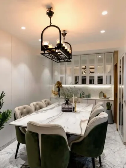 A beautifully appointed dining area featuring a marble-topped table, plush velvet chairs, and a modern chandelier. The mirrored cabinetry in the background adds depth and reflects light.