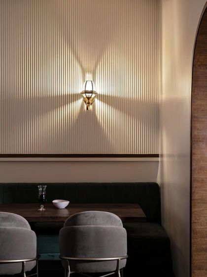 Lighting is not just for illumination; it's a design element. This brass wall sconce casts a beautiful starburst pattern against the vertically fluted wall, adding a touch of drama and elegance to the seating area.