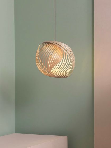 The Adilo pendant is shown in a corner, its warm light creating a cozy and inviting nook. The lamp's sculptural form adds an artistic element to the minimalist space.