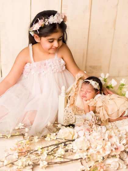 An older sister watches over the newest member of the family. The soft textures and floral elements create a fairytale-like newborn portrait.