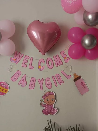 A simple wall decoration for a 'Welcome Baby Girl' celebration, using a banner, a heart-shaped balloon, and themed cutouts.