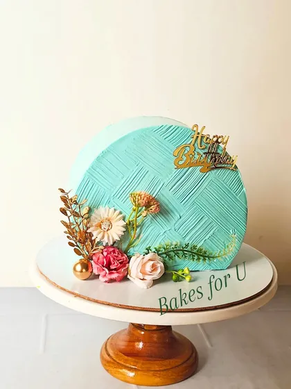 A modern cake-top-forward design with a textured turquoise finish. The cake is elegantly decorated with dried flowers and gold accents.