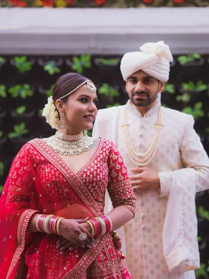 A candid moment between the bride and groom. Her makeup is fresh and luminous, with a special focus on the soft, rich tones of her eye makeup to complement her red lehenga.