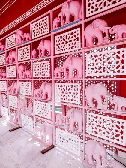 A unique decor element: a wall shelf filled with dozens of pink elephant statues, adding a playful and thematic touch to the Mehendi celebration.
