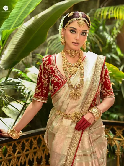 A full-view bridal shot against a lush, green backdrop. The model's pose on the balcony feels regal, and the contrast between the red blouse and green leaves makes the image vibrant and rich.