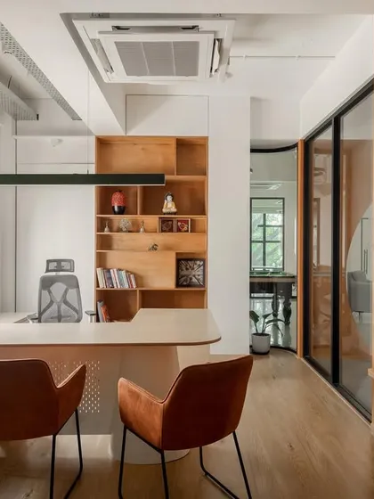 A director's cabin at Hosachiguru, designed with glass walls to maintain the sense of openness and transparency. The room features a custom desk, built-in wooden shelving, and warm, functional lighting.