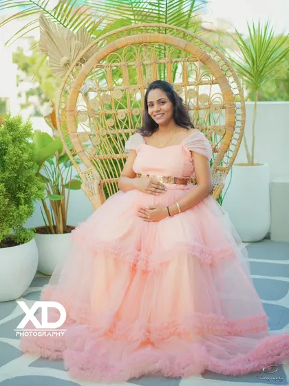 An elegant solo portrait of the mother-to-be seated in a chic peacock chair in a bright studio.