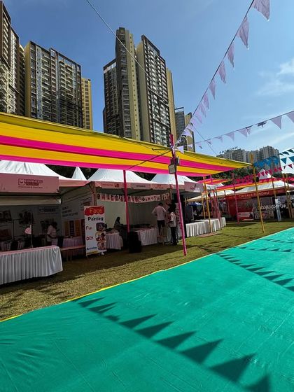 A wide view of the Kukdukoo Pune festival grounds against the city skyline. I handled the entire infrastructure, including the vibrant yellow and pink drapes, vendor tents, and ground covering, transforming an urban space into a festive playground.