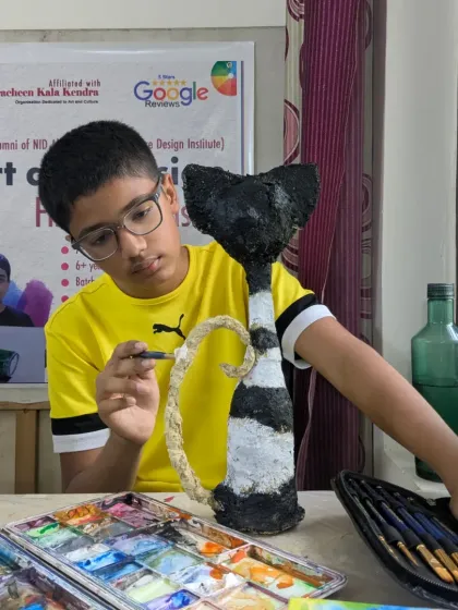 It's all about the process. Here, a young artist is completely absorbed in painting the final details on his papermache cat sculpture, learning patience and precision along the way.