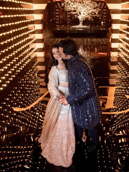 Natasha and Pranshu in a tunnel of lights at their sangeet. Her sparkling silver lehenga and his deep blue sherwani are a perfect match for a glamorous evening.
