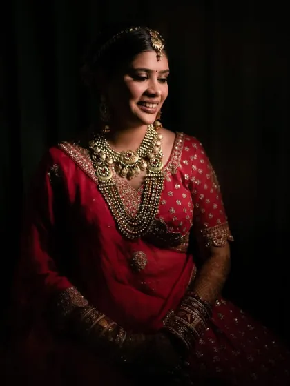A dramatic, shadowed shot of Pooja's bridal look. It highlights the richness of her attire and the flawless finish of her makeup.