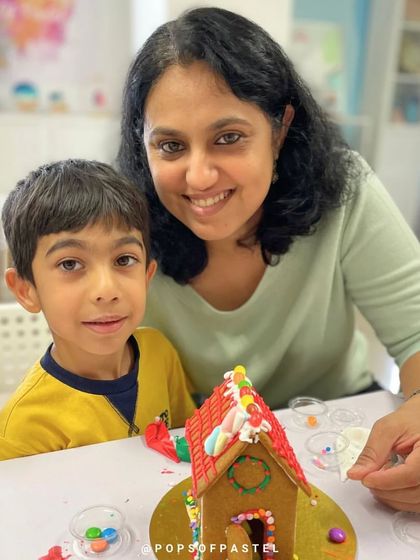 A mother and son duo proudly pose with their finished gingerbread house, a sweet memory from our holiday workshop.