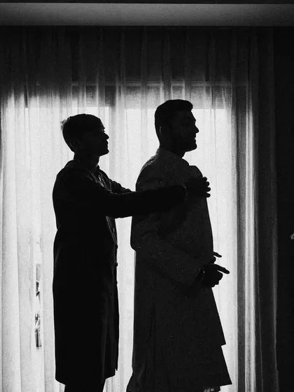 A silhouetted shot of the groom getting ready with the help of a family member. It’s a simple, powerful image about family and tradition.