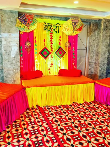 A complete Mehendi seating arrangement with a main divan and side seating, all coordinated with a colourful backdrop.