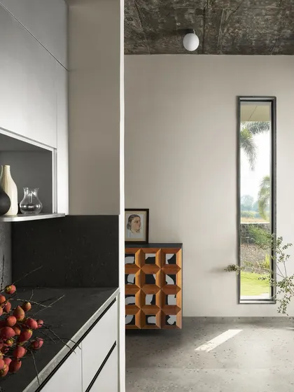 Another view of the kitchen and entry at Pavilion House, showcasing the clean lines and material contrast. The sleek white cabinetry is set against a dark stone countertop, while a geometric wooden console stands as a functional art piece.