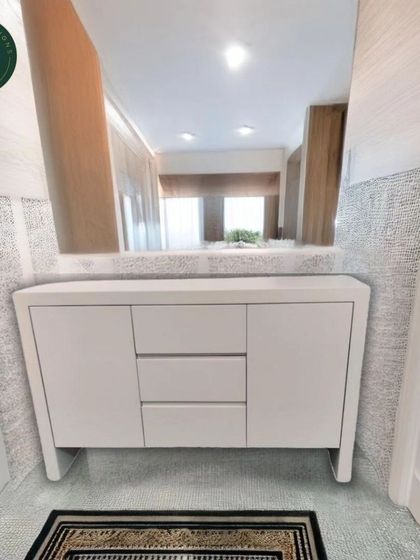The white minimalist sideboard shown in an entryway, reflecting in a large mirror. Its simple design allows it to blend seamlessly into any modern space.