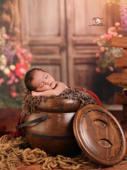 Using unique props can create magical images. Here, a newborn sleeps peacefully atop a rustic wooden pot, surrounded by a soft, floral backdrop that adds a touch of enchantment to the portrait.