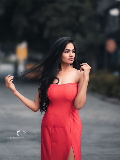 A striking outdoor portrait in a vibrant red dress. The wind catching her hair adds a sense of movement and drama to this elegant look.