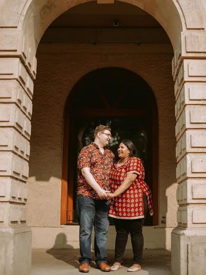 A beautifully framed shot of a couple standing in an archway, holding hands and sharing a look of love.