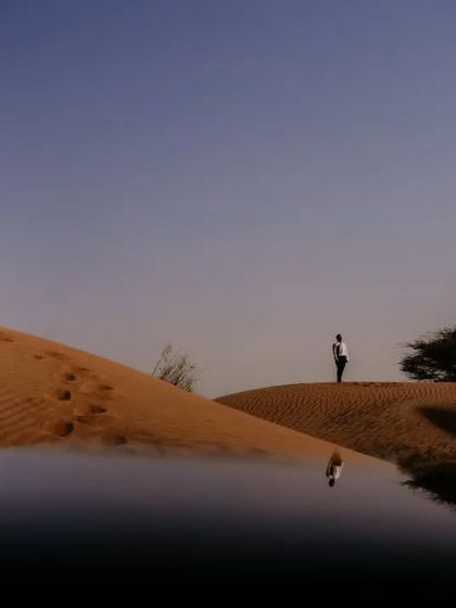 A surreal and artistic photograph in the Abu Dhabi desert, using a water reflection to create a stunning mirage effect. This shot highlights our creative approach to landscape and destination couple photography.