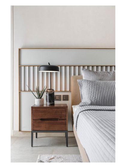 A wider view of the guest bedroom, showing the custom headboard, dark wood nightstand, and modern table lamp.