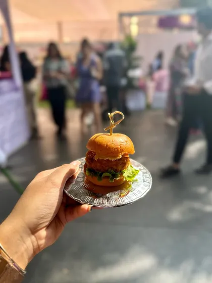 A hand holding a mini slider, part of the delicious spread at the Luxe Shopping Experience pop-up event.