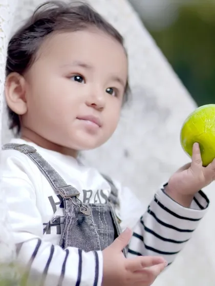 A close-up portrait of a child holding a small green ball, with a soft, natural background that makes the subject stand out.
